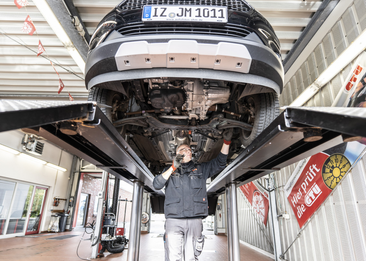 Ein Mechatroniker untersucht ein Auto unter einer Hebebühne.