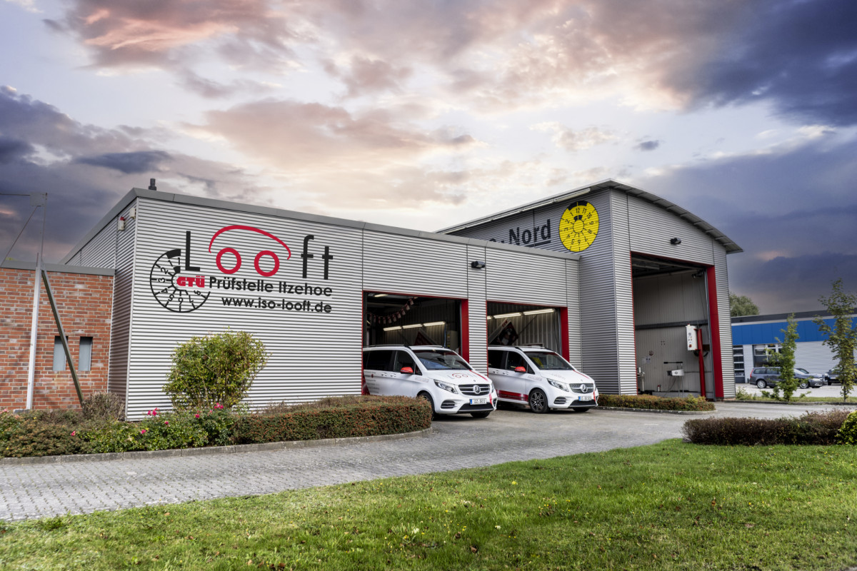 Außenansicht eines großen Firmengebäudes mit Firmenfahrzeugen vor den geöffneten Toren. Auf dem Gebäude steht: „Looft GTÜ Prüfstelle Itzehoe“